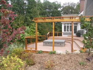 A pergola and deck setup with a curved layout design to fit a hot tub inset. For the best deck builders in Rockford MI has to offer, call Signature Decks & Construction
