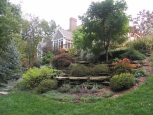 Signature creates luxury decks, sunrooms, and landscaping that is unique to each home. A custom multi-tiered landscaping project with grass, stone, shrubs, two flower beds and a tree near Ada, MI.