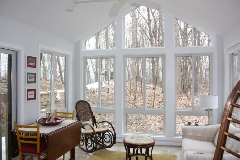 The interior, painted white, overlooking a wooded area in fall in a four seasons room built by Signature Decks & Construction