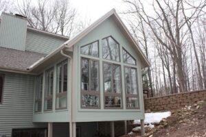 A sunroom addition extending from a woodland house. The sunroom was made by Signature Decks & Construction and features a vaulted cathedral ceiling.