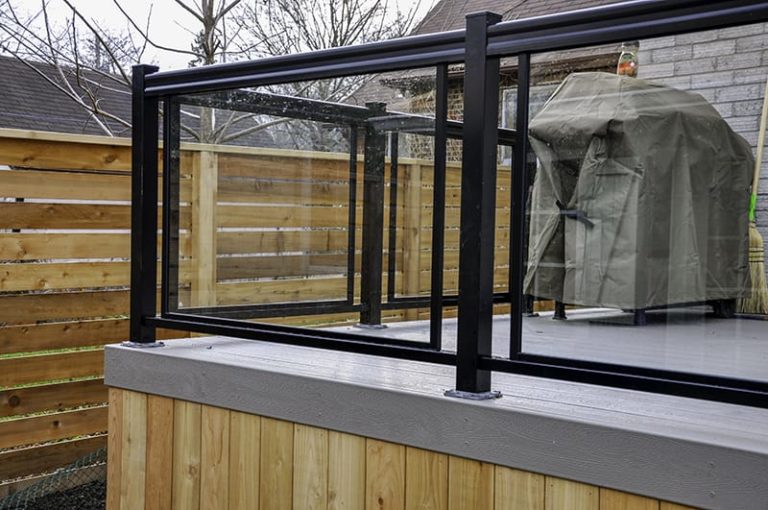 Glass panels along railings are just one example of outdoor deck decor that you can add to a Signature Decks project. Glass sits framed inside a black mounted railing.