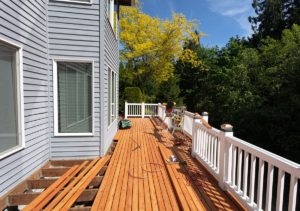 A deck repair in progress. New wood planks being installed on an elevated wrap around deck with white guard rail.