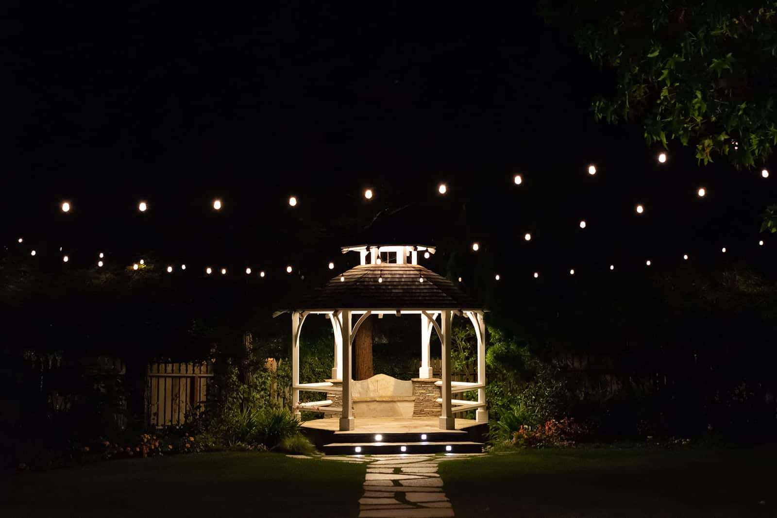 Patio lighting ideas take many forms, including (as shown) string lights around a Gazebo at night, or lights within the steps of a walkway.